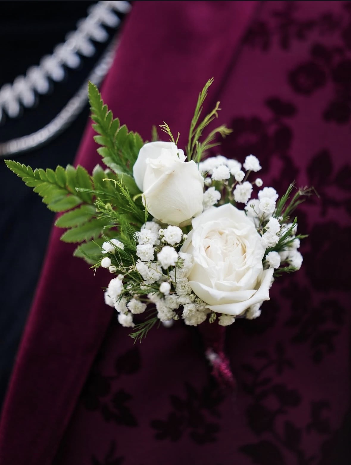 White rose boutonniere detail on burgundy suit